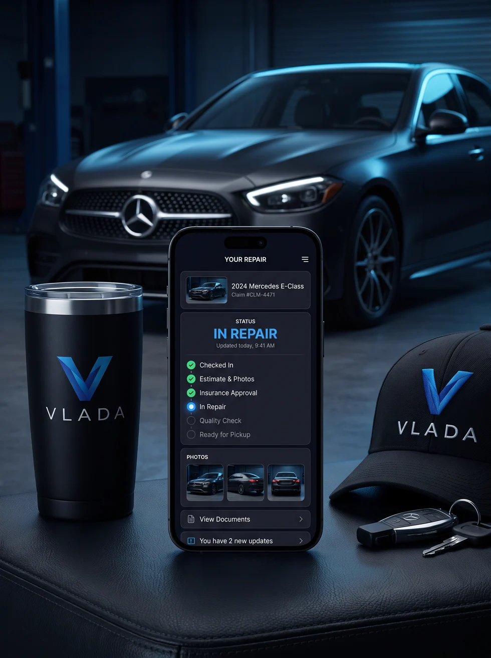 VLADA customer portal on a phone between branded VLADA tumbler, cap and car keys in an auto body shop